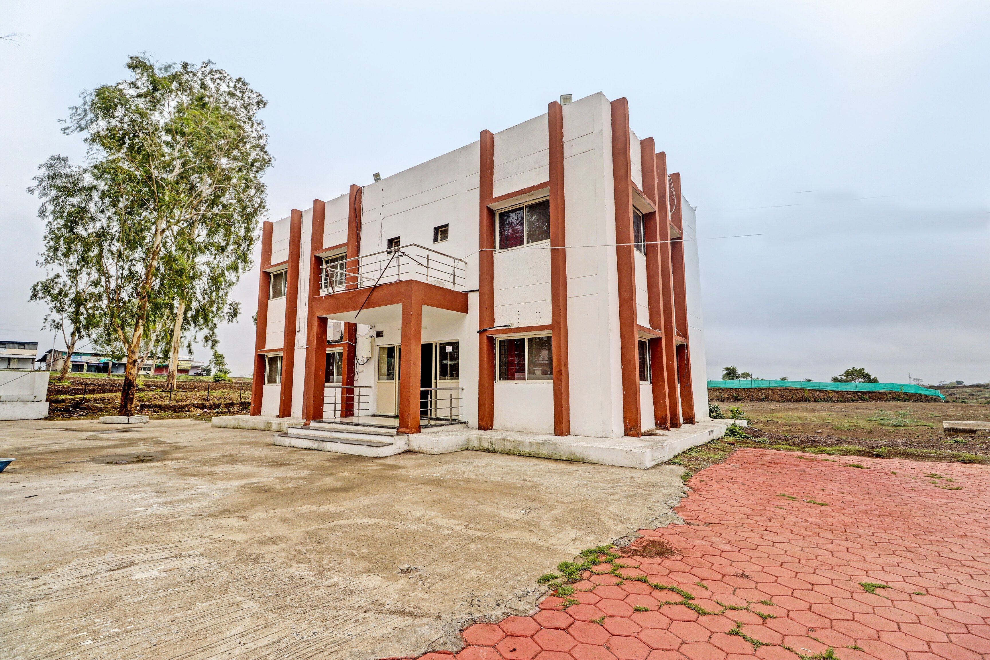 A modern two-story building with a flat roof, a balcony on the second floor, and a paved entrance area.