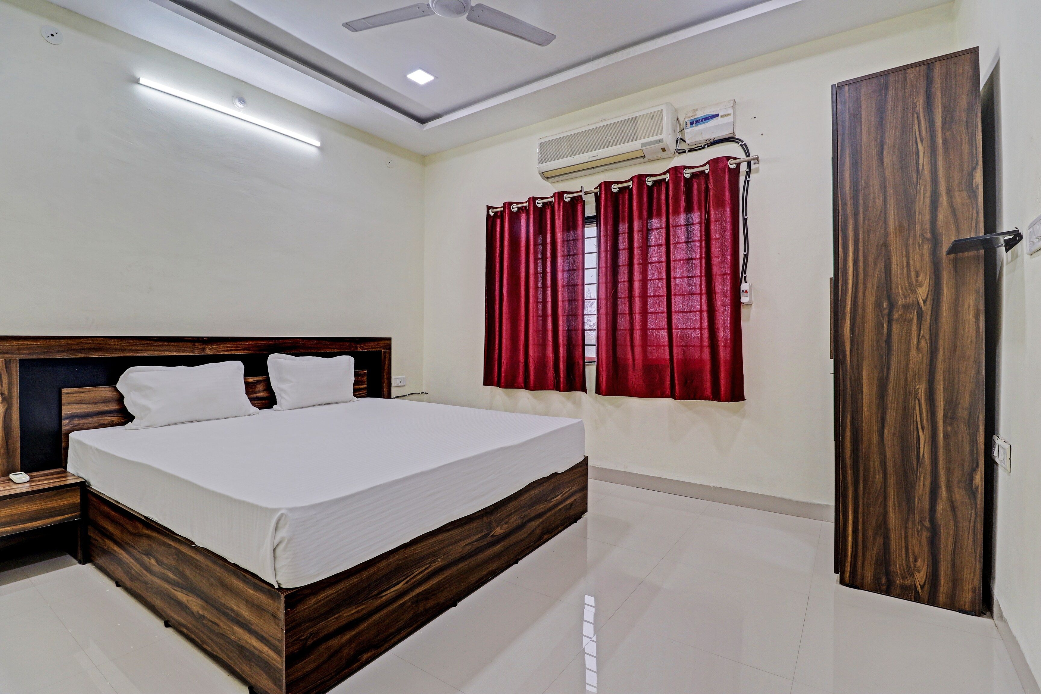 A bedroom with a wooden bed, a nightstand, a ceiling fan, an air conditioning unit, and a door.