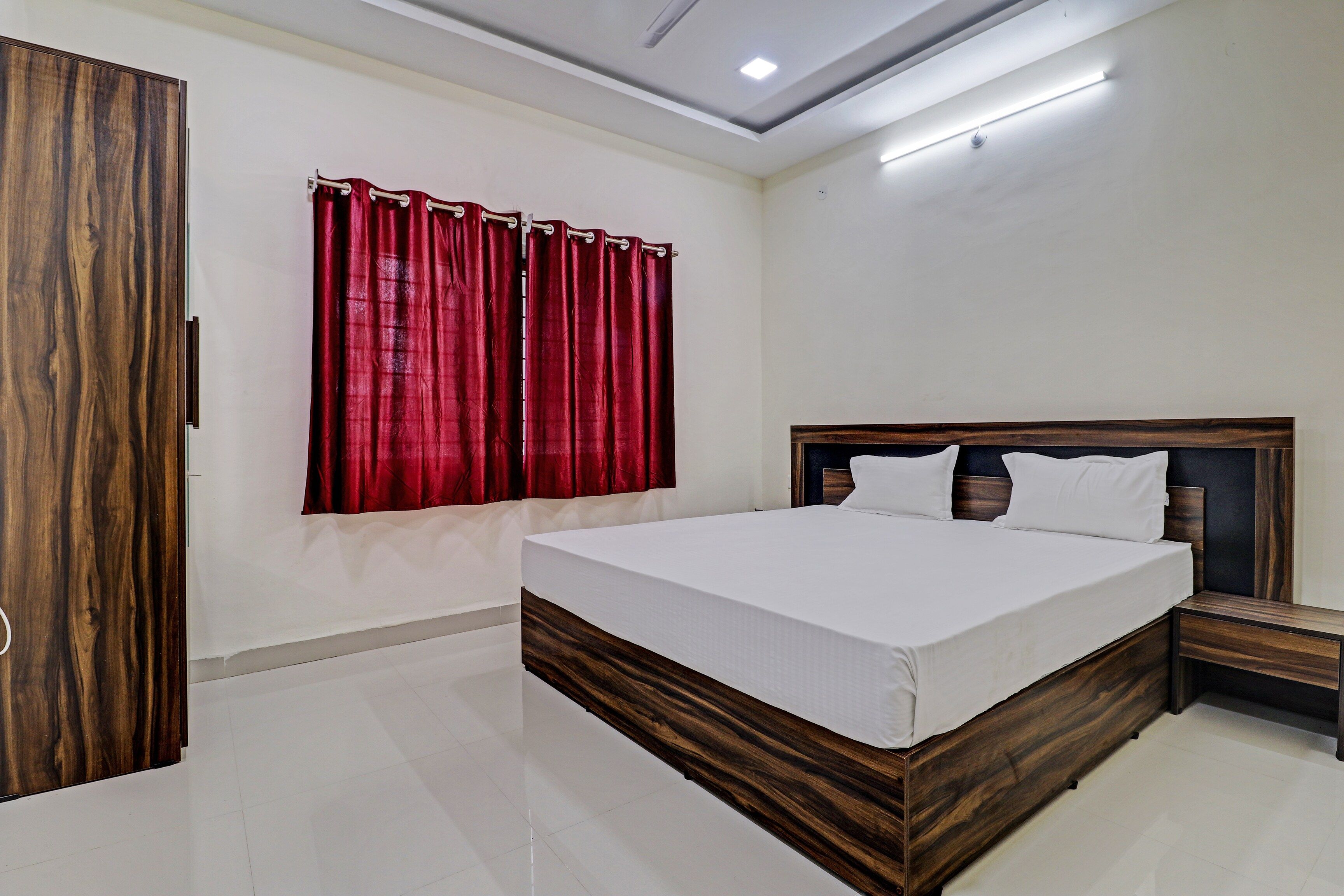 A bedroom with a wooden bed frame, white bedding, a nightstand, and a wardrobe.