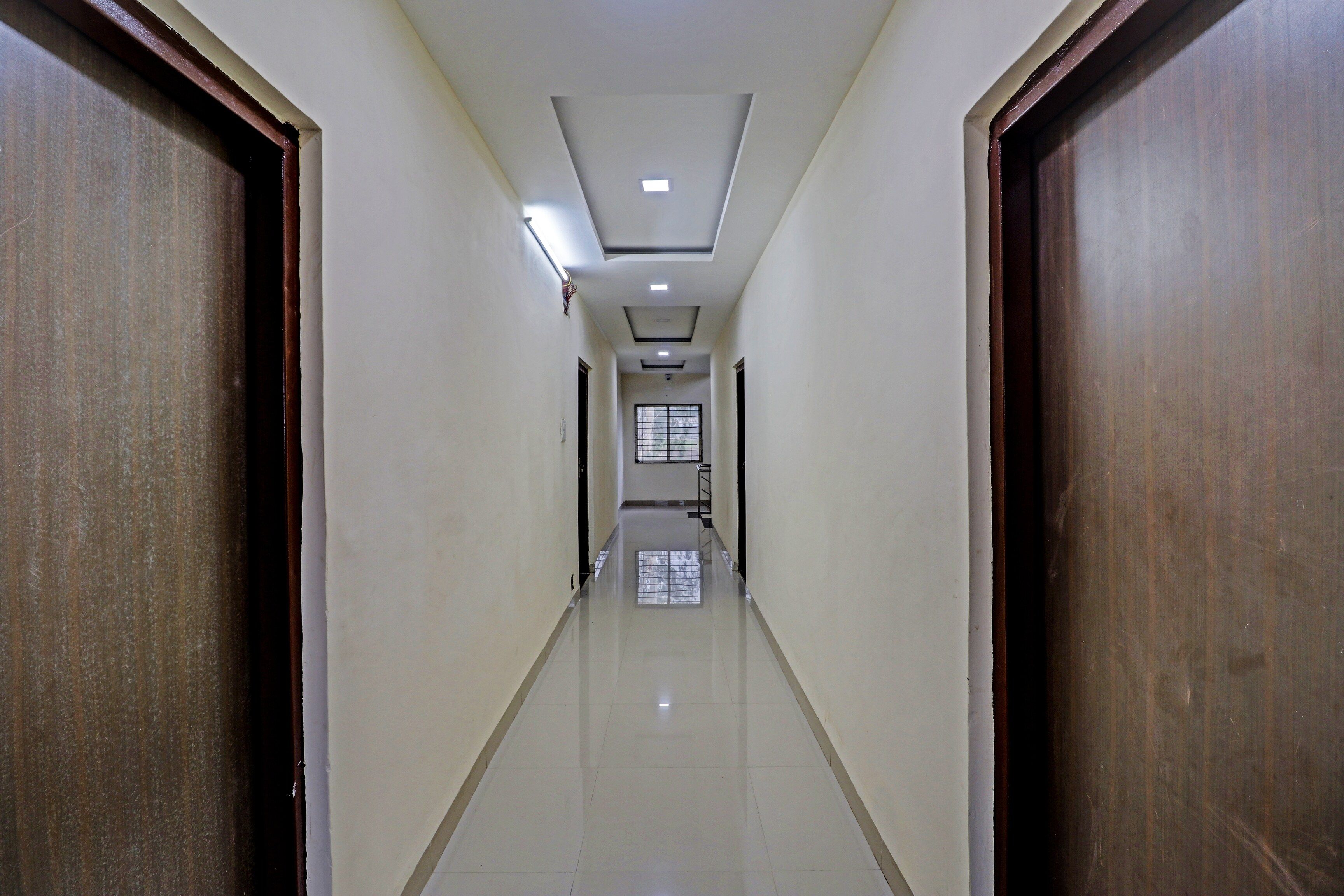 A corridor with a tiled floor, wooden doors, and a ceiling with recessed lighting.