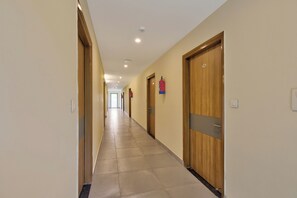 A long, narrow hallway with wooden doors on one side and a fire extinguisher mounted on the wall. - Super Hotel O Blessings Residency (Dehradun)