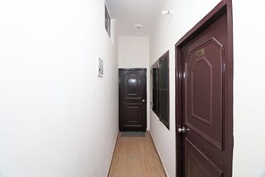 A narrow hallway with a wooden floor, white walls, and two doors, one with a number plate. - Hotel O Mahalaxmi Palace (Dehradun)