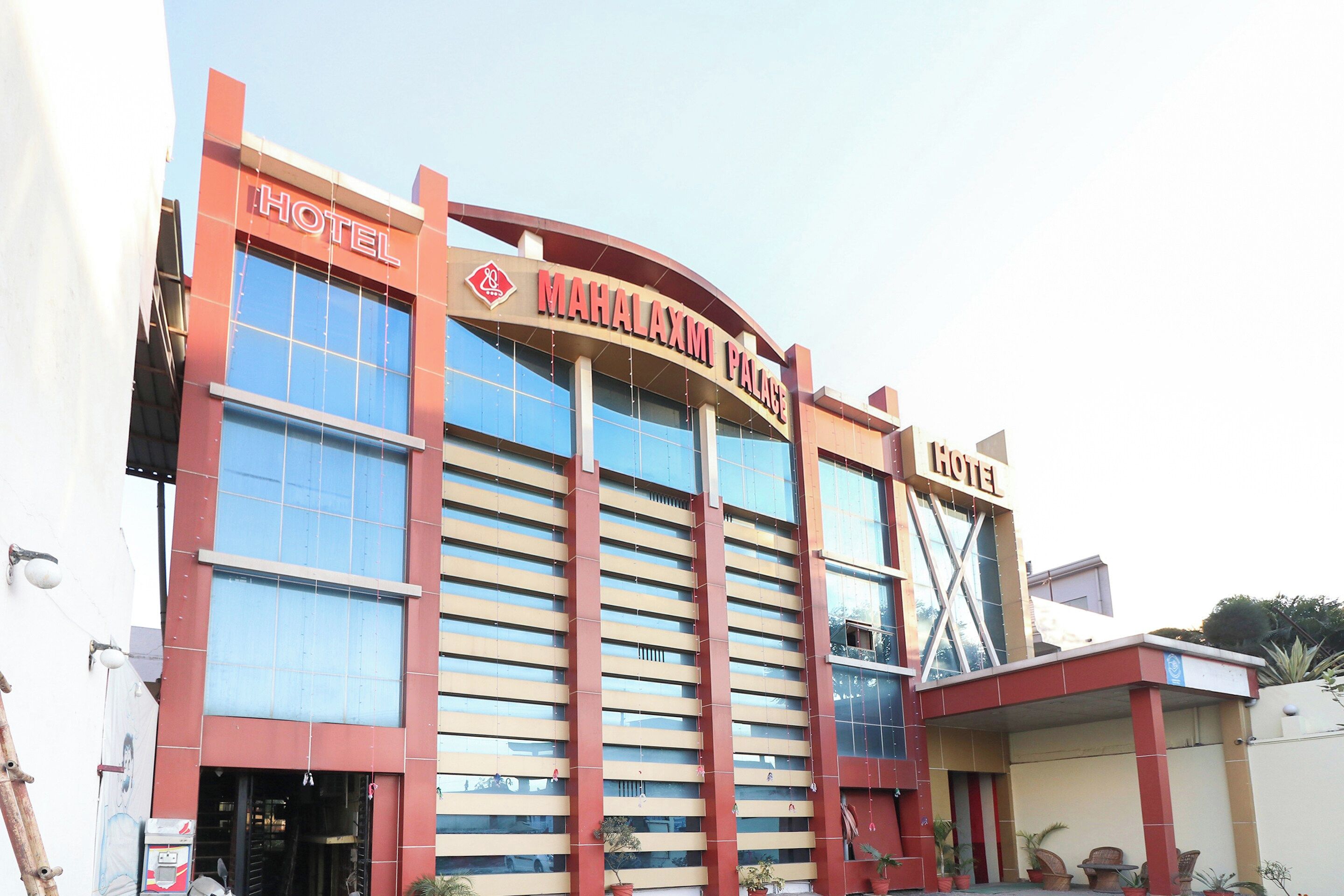 Un hôtel reconnaissable à son enseigne bien visible, portant l’inscription « MAHALAXMI PALACE HOTEL », et à sa grande façade en verre.