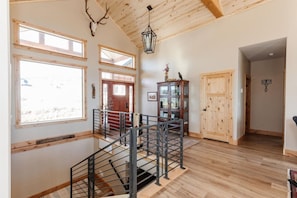A spacious interior with a wooden staircase, large windows, and a high ceiling.