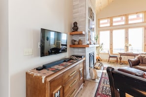 A living room with a flat-screen TV, wooden cabinets, a fireplace, and a dining area with natural light.