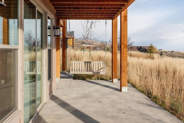 A covered porch with a bench, wooden pillars, and a view of a grassy field.