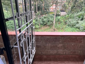 Un balcon doté d’une grille en métal, d’un mur en briques et offrant une vue sur la verdure et les bâtiments qui se dressent à l’arrière-plan.