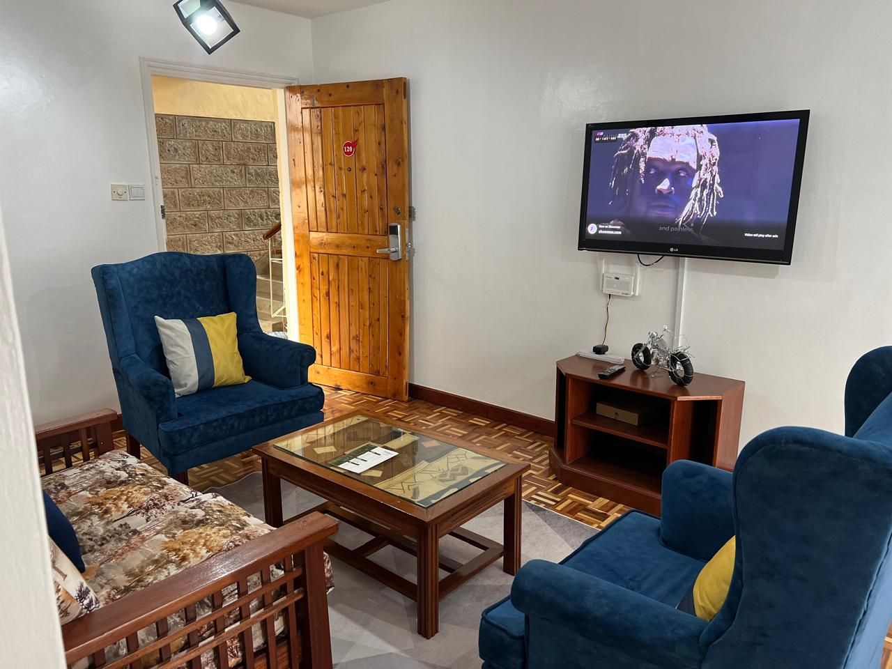 Un salon avec deux canapés bleus, une table basse en verre et un téléviseur fixé au mur.
