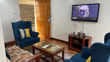 Ein Wohnzimmer mit zwei blauen Sofas, einem Glastisch und einem an der Wand befestigten Fernseher.