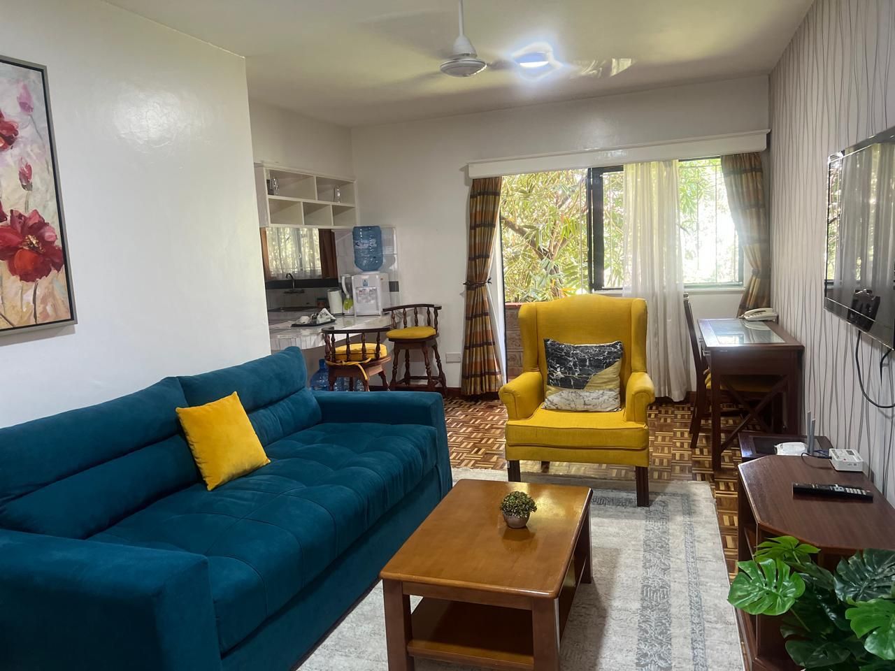 Un salon avec un canapé bleu, un fauteuil jaune, une table basse en bois et un coin repas comprenant une table et des chaises.