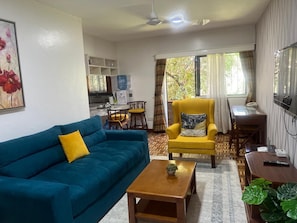 Un salon avec un canapé bleu, un fauteuil jaune, une table basse en bois et un coin repas comprenant une table et des chaises.