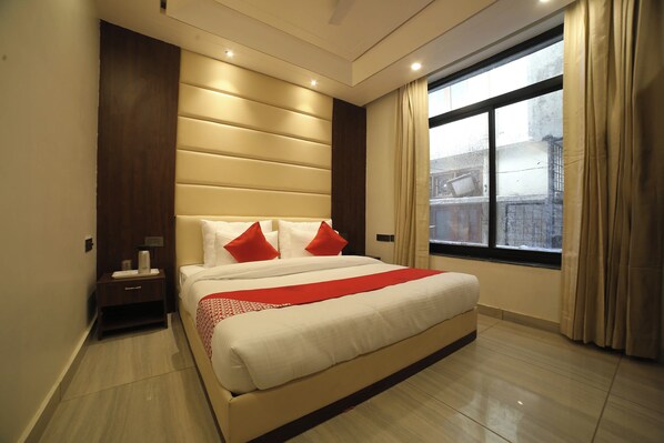 Quarto de hotel com uma cama grande, mesa de cabeceira, janela com cortinas e vista exterior.