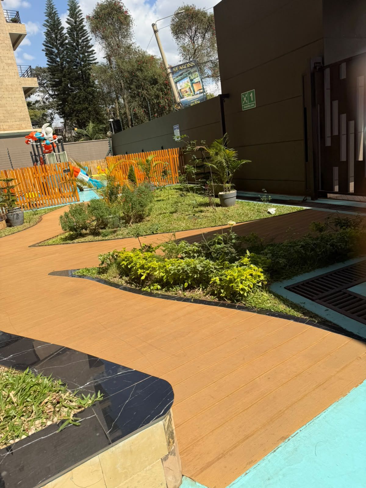 Une cour avec une terrasse en bois, des plantes en pot et un espace de jeux clôturé.