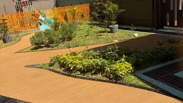 Une cour avec une terrasse en bois, des plantes en pot et un espace de jeux clôturé.