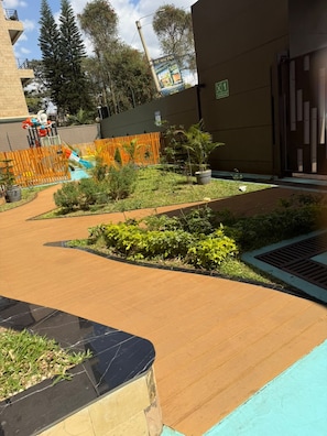 Une cour avec une terrasse en bois, des plantes en pot et un espace de jeux clôturé.