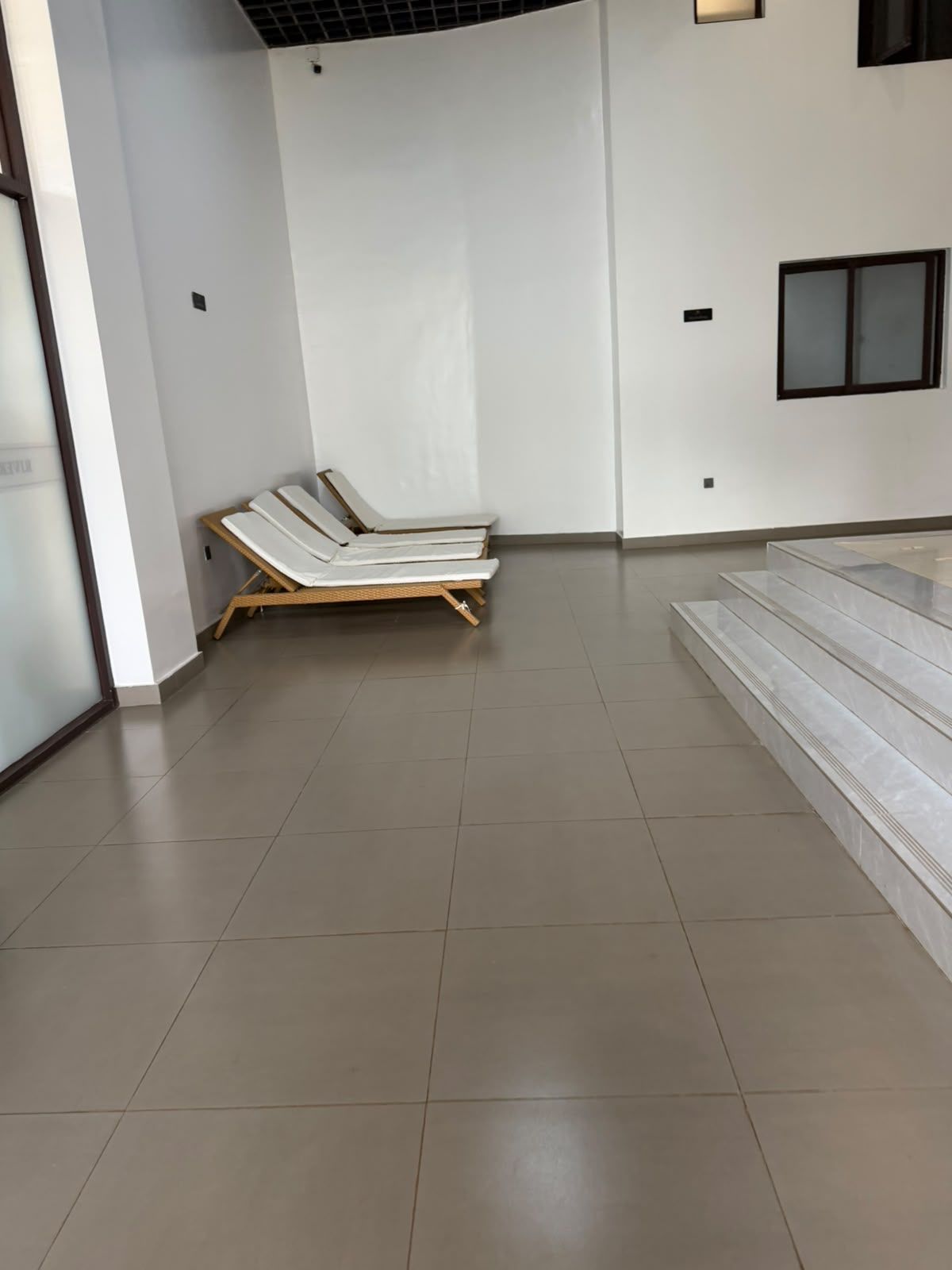 Une pièce avec un sol carrelé, un escalier et une rangée de chaises longues adossées à un mur.