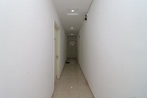 A narrow, well-lit hallway with white walls and a tiled floor, leading to a door at the end. - Hotel O Happy Feet Guest (Dehradun)
