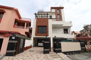 A modern two-story building with a gated entrance, a balcony on the upper floor, and a visible car parked in the driveway. - Hotel O Happy Feet Guest (Dehradun)