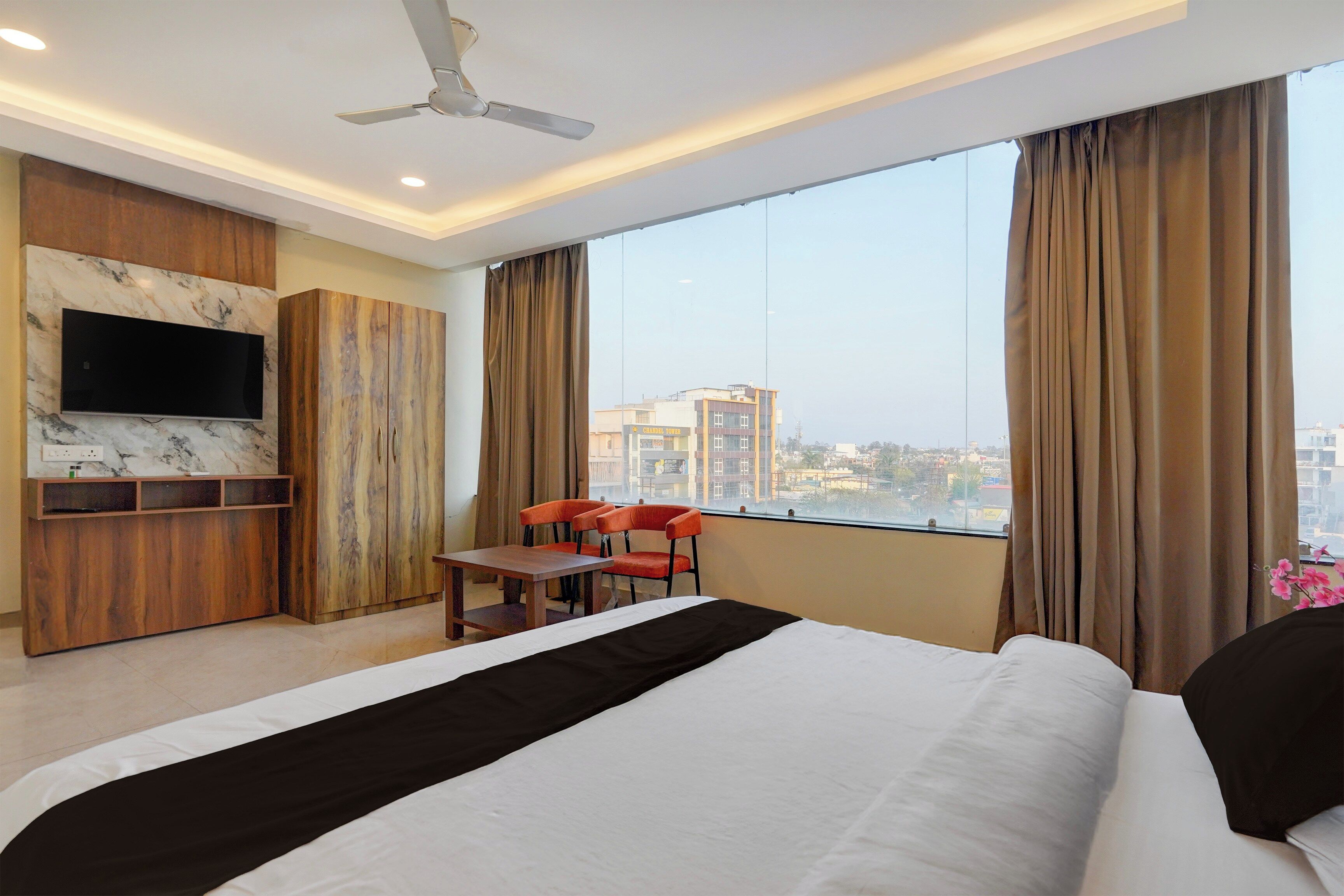 A hotel room with a bed, a desk, a chair, a TV, and a large window with curtains.