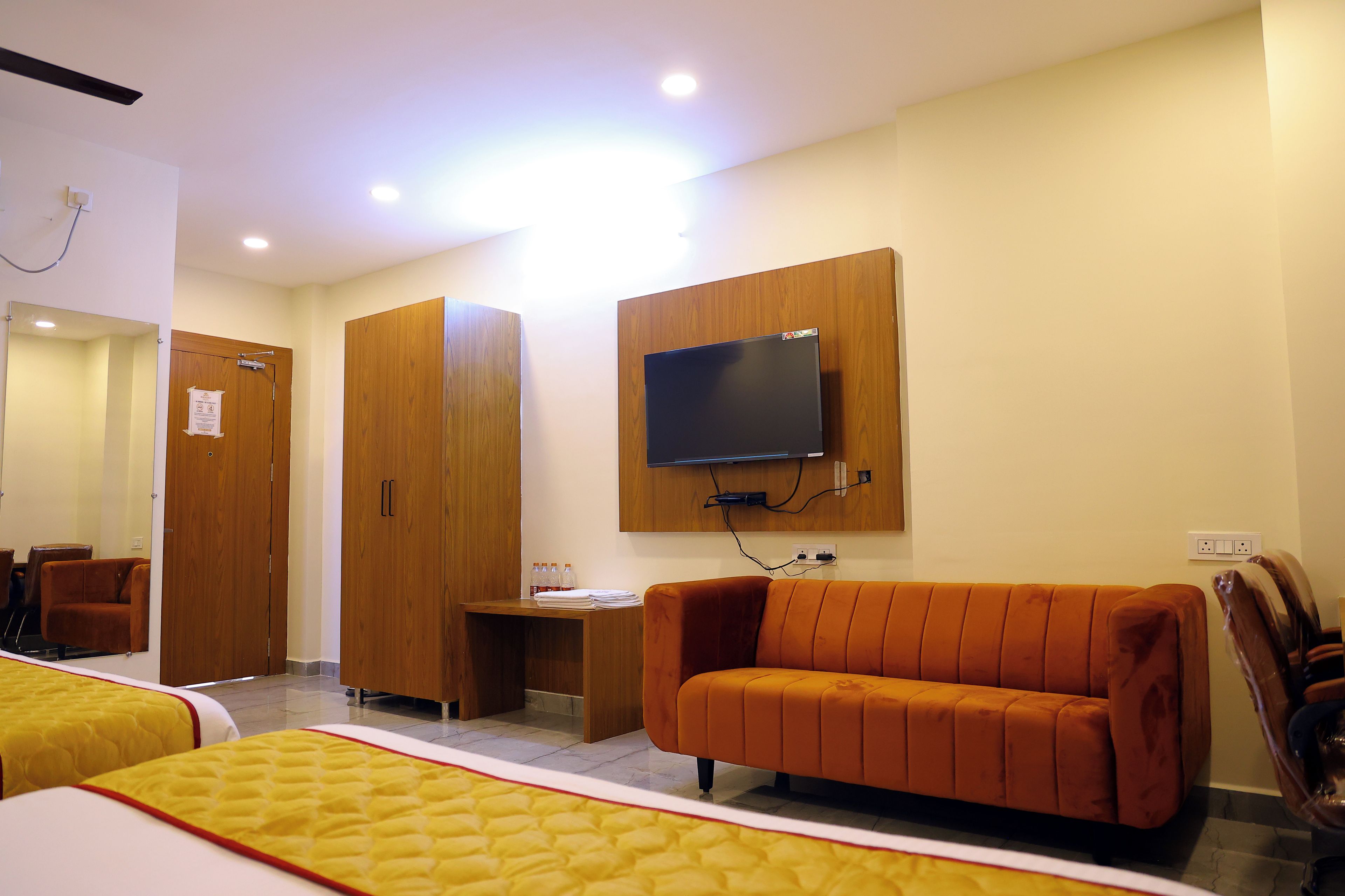 A hotel room with a bed, a sofa, a TV mounted on the wall, and a mirror.