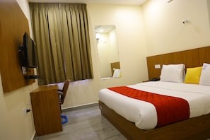A hotel room with a bed, a desk, a television, a mirror, and a window with curtains. - Mahant Hotel (KANIGIRI)