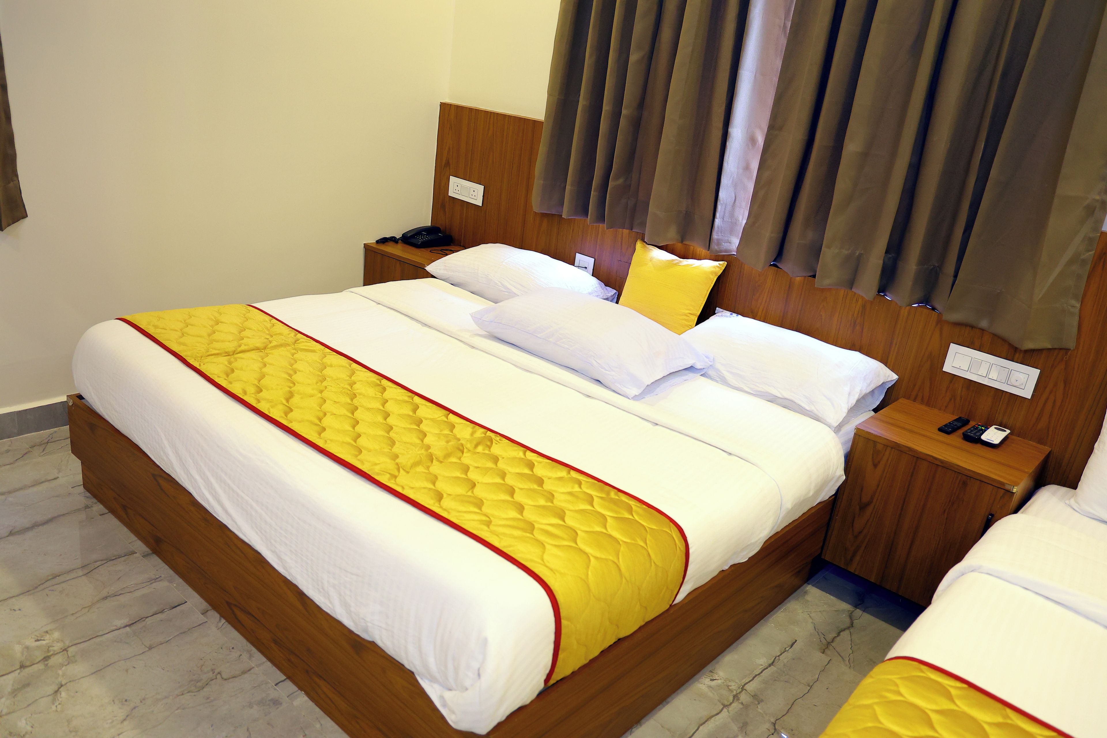 A hotel room with a large bed, wooden headboard, a bedside table with a phone, and a nightstand with a lamp.