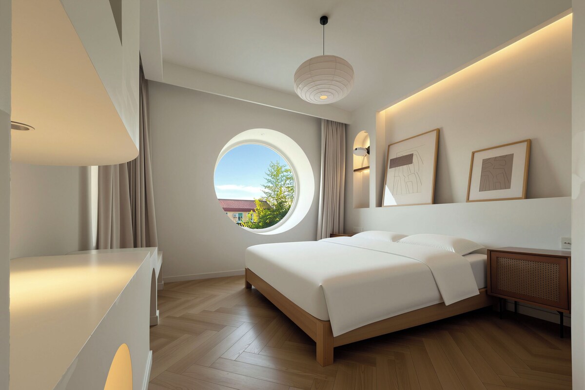 Un dormitorio moderno con una cama grande, un ventanal redondo y vistas al exterior.