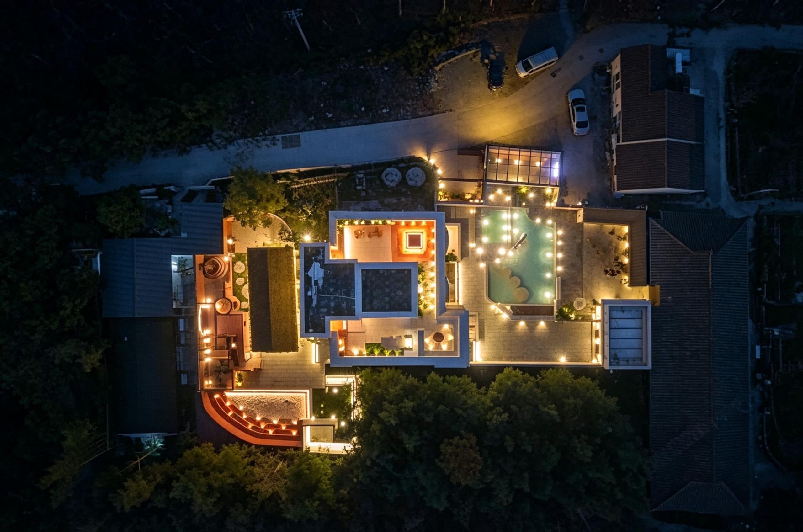 Vista aérea de una propiedad residencial con piscina, iluminación exterior y camino de entrada.