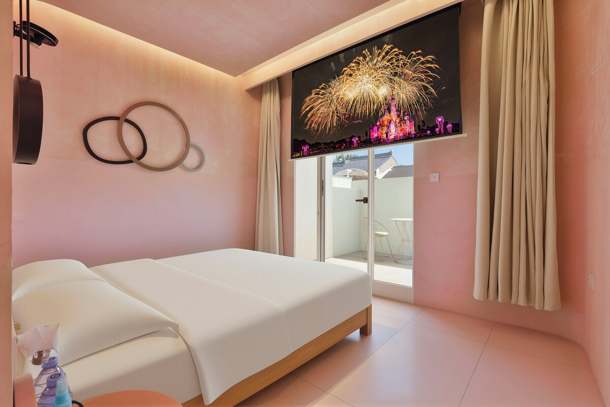 Habitación de hotel moderna con cama, televisión de pared mostrando fuegos artificiales y vistas al exterior.