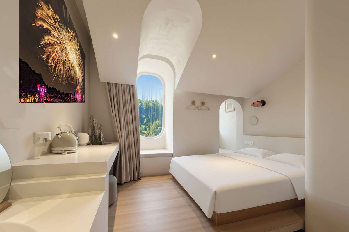 Una habitación de hotel moderna con cama, mesita de noche y ventana con vistas.