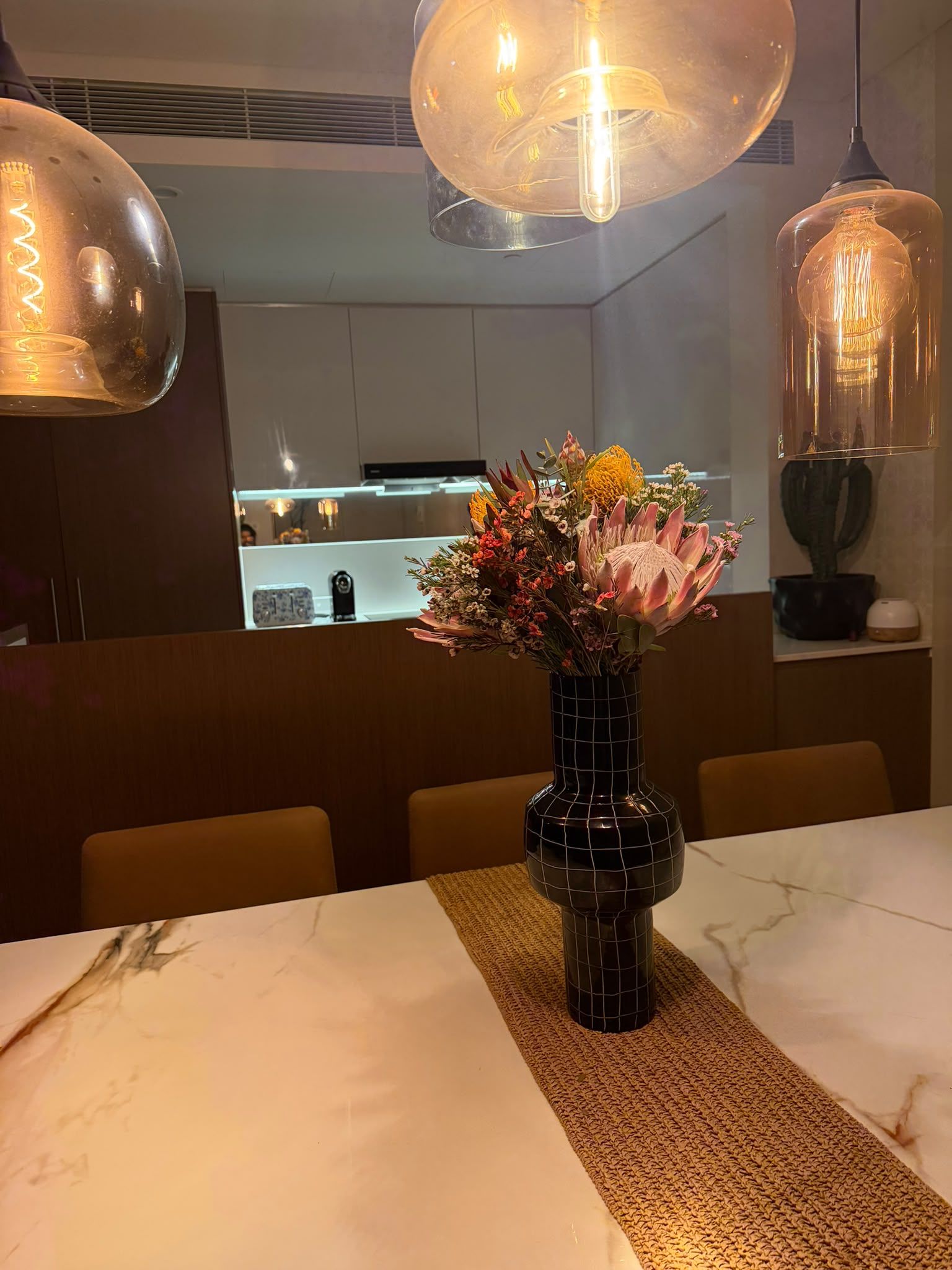 Un comedor con una mesa de mármol, un jarrón con flores e iluminación colgante.