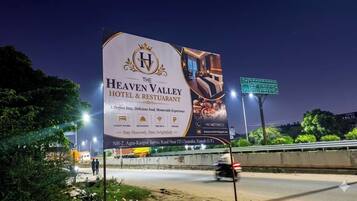 Une grande affiche publicitaire pour l’hôtel-restaurant The Heaven Valley, qui met en avant ses nombreux avantages, notamment des chambres de luxe, un restaurant, une connexion Wi-Fi gratuite et un parking.