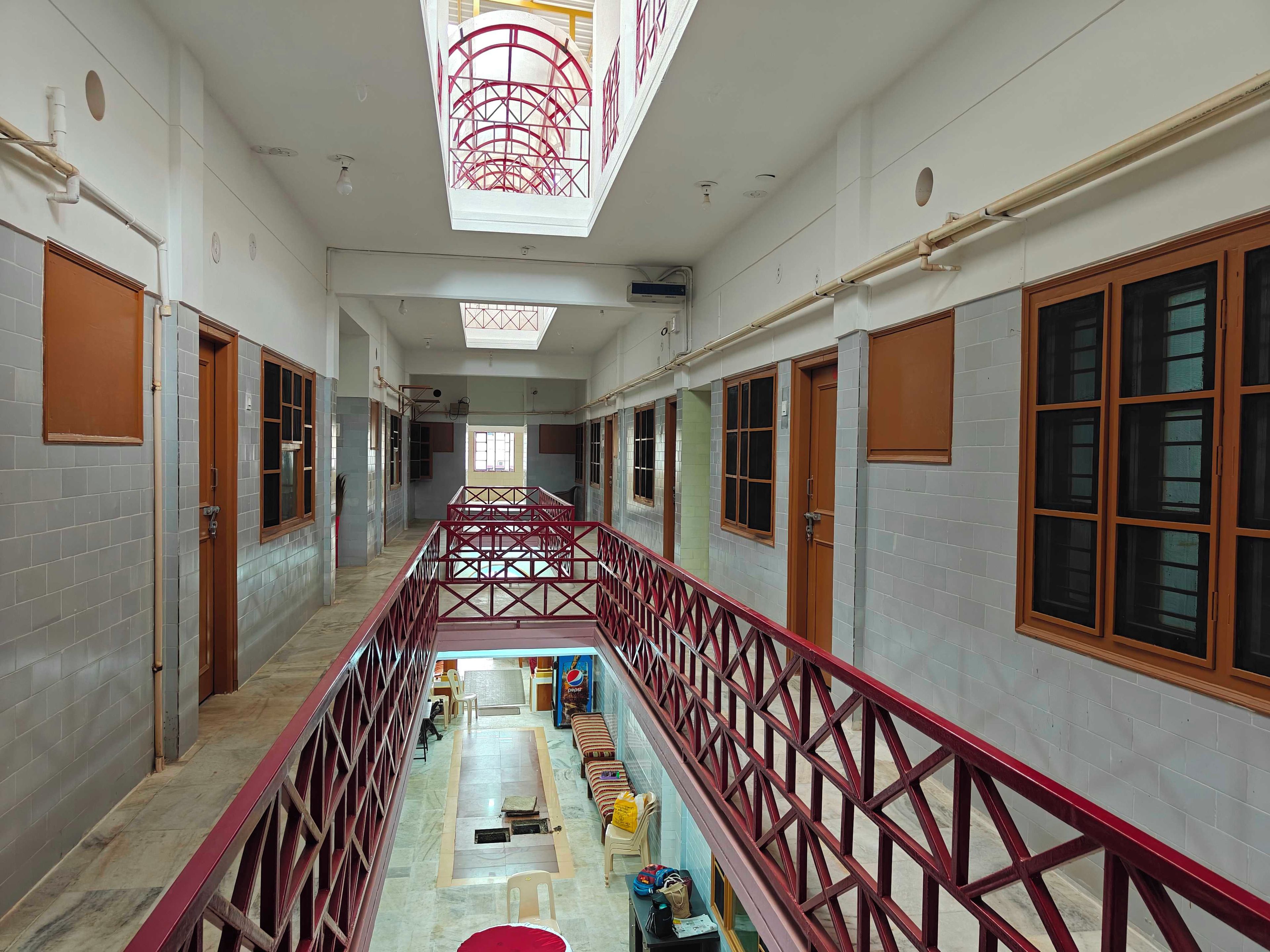 A hotel corridor with a central walkway, wooden doors, and a red railing.