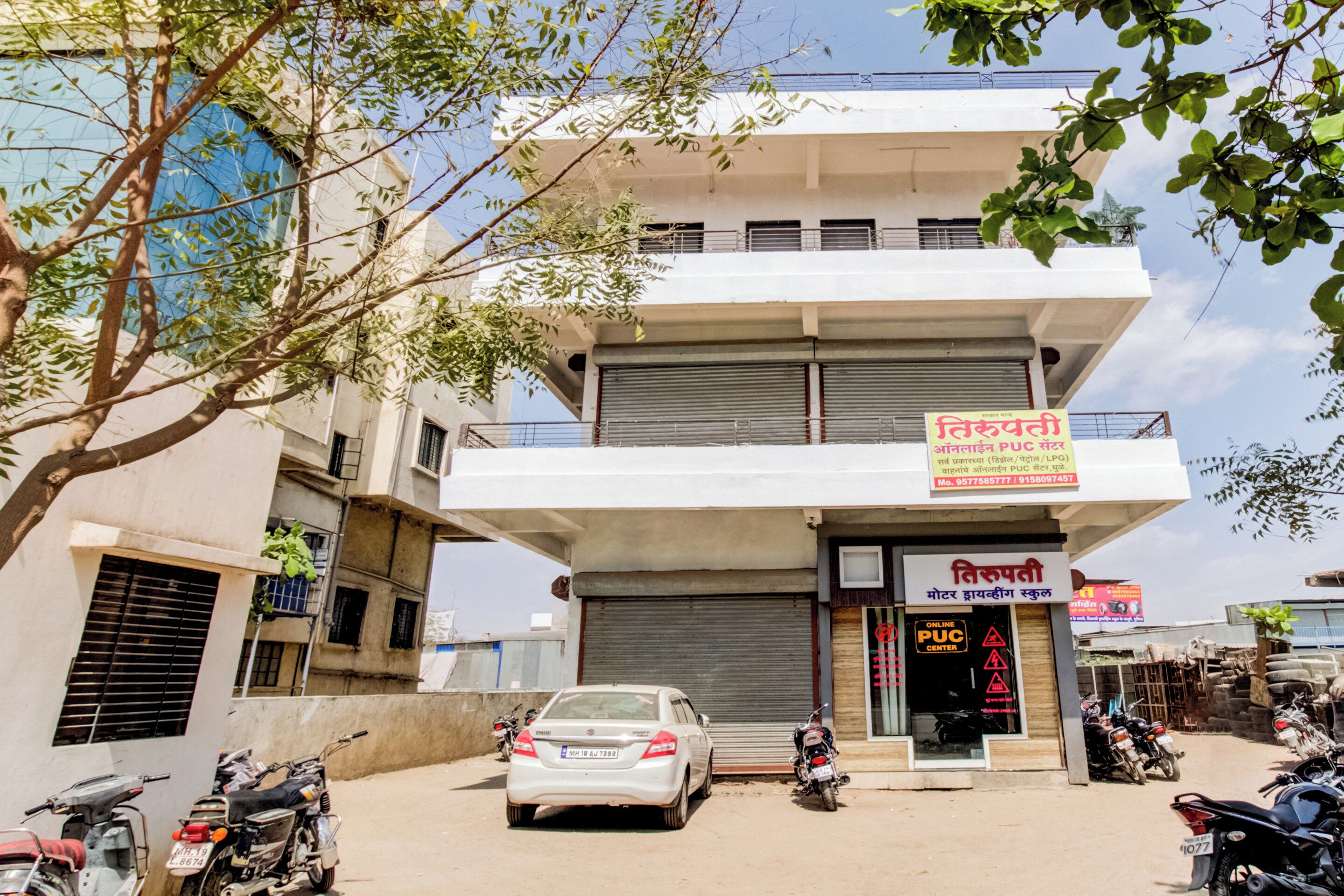 Un edificio de varios pisos con un toldo cerrado en la planta baja, un letrero de una escuela y varios vehículos estacionados.