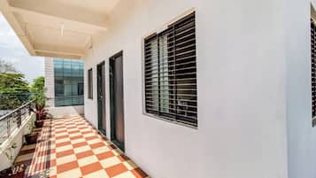 A covered balcony with checkered flooring, potted plants, and a view of a modern building.