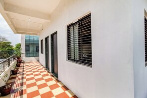 A covered balcony with checkered flooring, potted plants, and a view of a modern building.
