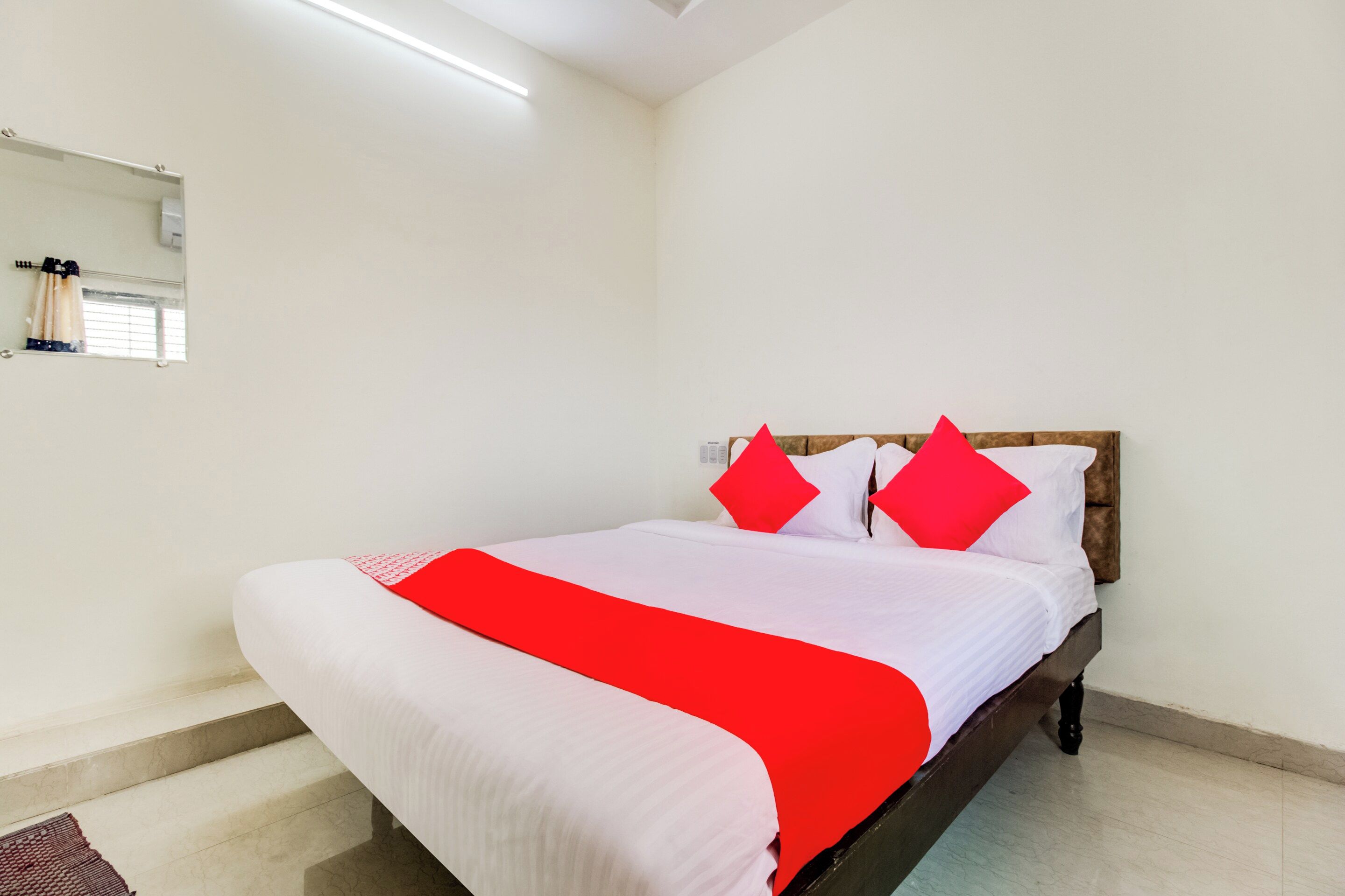 A neatly made bed with a white and red bedspread, a wooden headboard, and two red pillows.