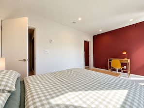 Ein Schlafzimmer mit einem Bett, einem Schreibtisch mit Stuhl und einer Tür zu einem anderen Raum.
