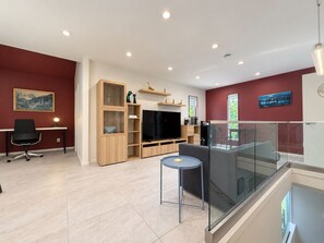 A modern living room with a flat-screen TV, wooden shelving, a glass railing, and a dining area with a chair and table. - Private 1BR Suite near Steveston | Living Room, No Kitchen (Richmond)