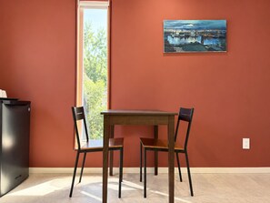 Ein Essbereich mit Tisch und Stühlen, einem Bild an der Wand und einem Fenster mit Blick auf Bäume.
