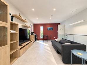 Ein modernes Wohnzimmer mit einem Flachbildfernseher, Holzregalen, einem grauen Sofa und einem kleinen Tisch.