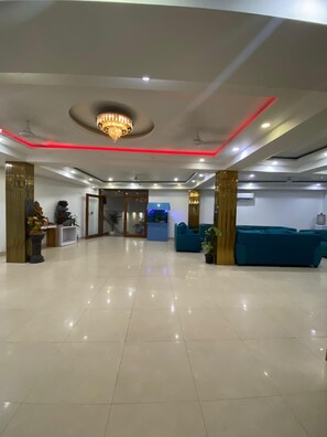 A spacious lobby with a reception desk, a chandelier, and a blue sofa. - Hotel Modesty - Mahipalpur Delhi (New Delhi)