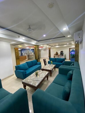 A modern living room with teal sofas, marble coffee tables, and a ceiling with recessed lighting. - Hotel Modesty - Mahipalpur Delhi (New Delhi)