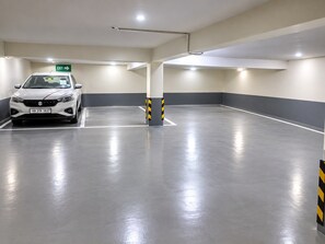 Eine Parkgarage mit einem weißen Auto in einem markierten Stellplatz, Hinweisschildern für den Ausgang und Säulen mit gelb-schwarzen Streifen.