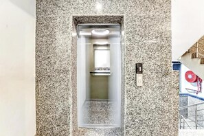 An elevator with a metallic interior and a granite wall surrounding it. - Hotel Modesty - Mahipalpur Delhi (New Delhi)