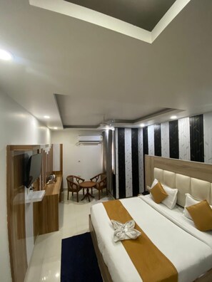 A hotel room with a bed, a desk with a TV, a chair, and a window with curtains. - Hotel Modesty - Mahipalpur Delhi (New Delhi)