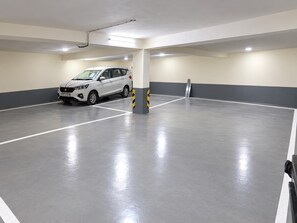 A parking garage with a white car parked in one of the bays. - Hotel Modesty - Mahipalpur Delhi (New Delhi)