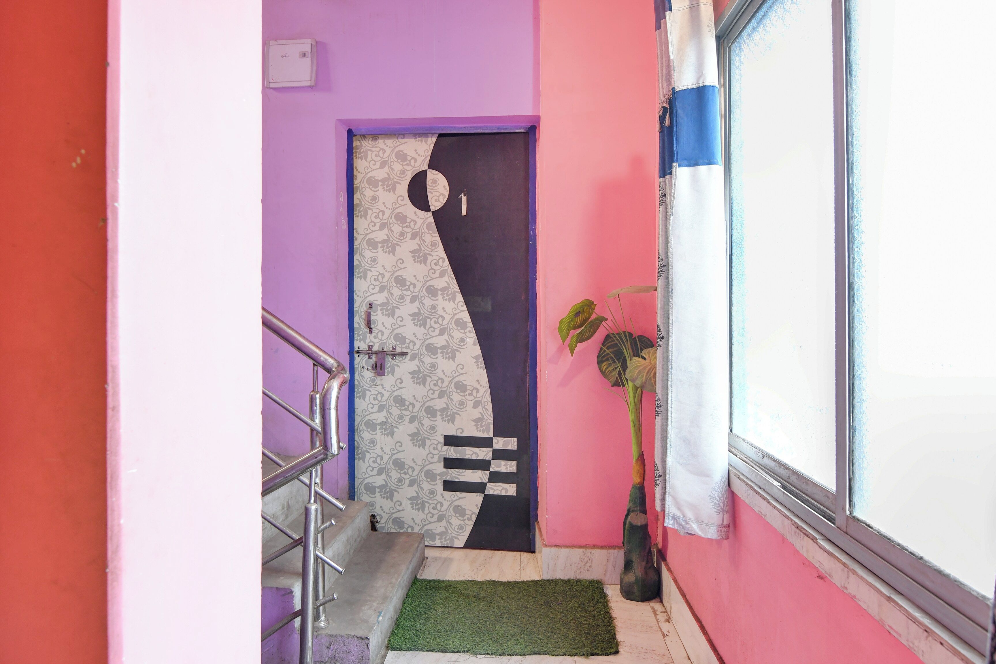 A hallway with a purple wall, a door with a geometric pattern, a metal staircase, and a potted plant.