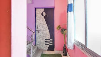 A hallway with a purple wall, a door with a geometric pattern, a metal staircase, and a potted plant.