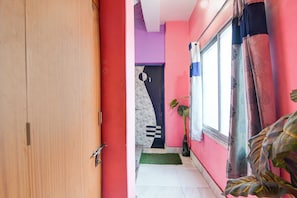 A narrow hallway with a wooden door on the left, a purple wall, and a window with curtains on the right.